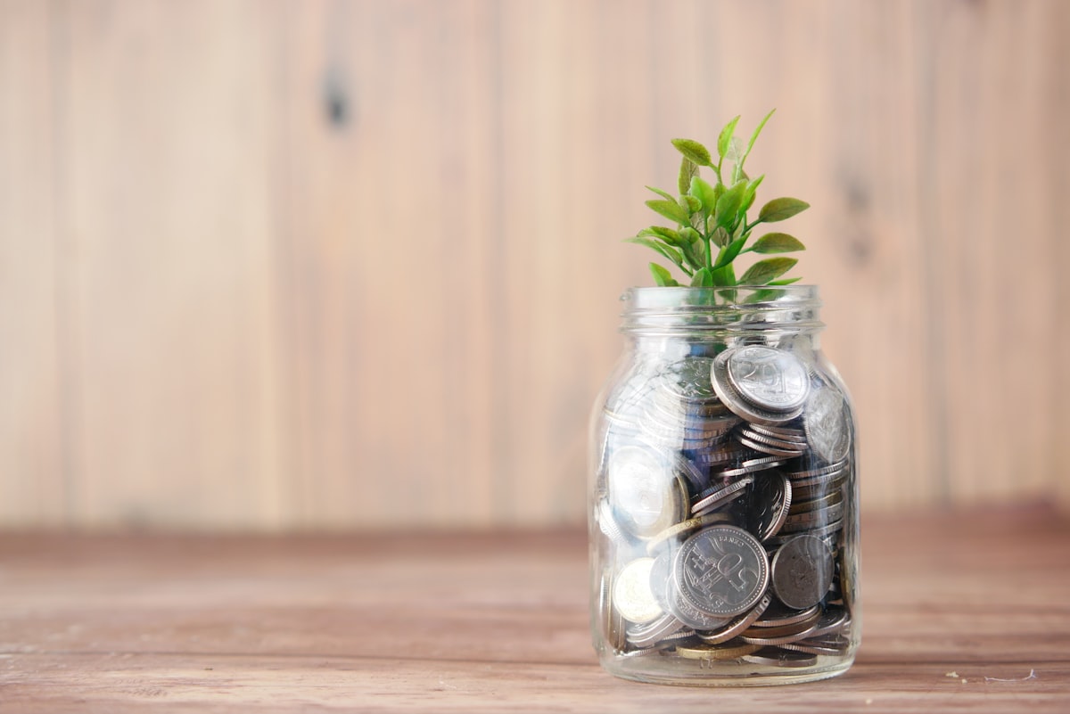 Glass jar of coins beside a growing plant symbolizing retirement savings